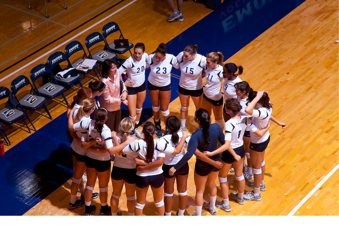 Emory University Volleyball players huddle before a game with their coach. 