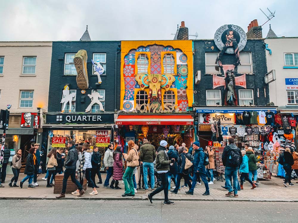 A crowd of people walking in front of graffitied buildings.